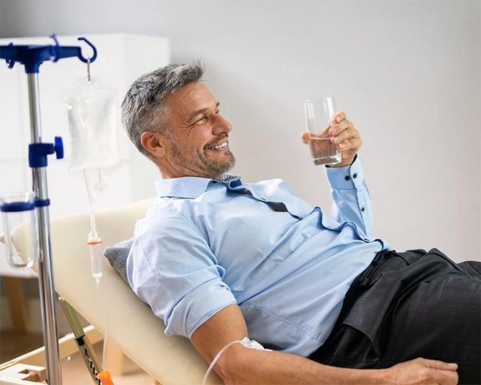 A man lying in a hospital bed drinks water